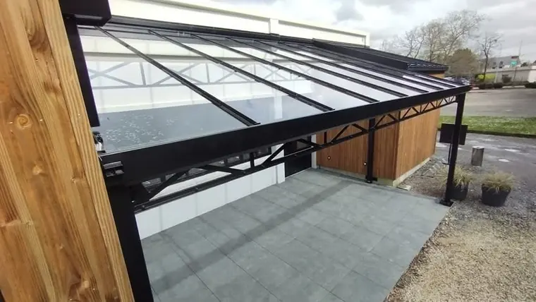 Toiture vitrée sur ossature acier noir au-dessus d'une terrasse dallée