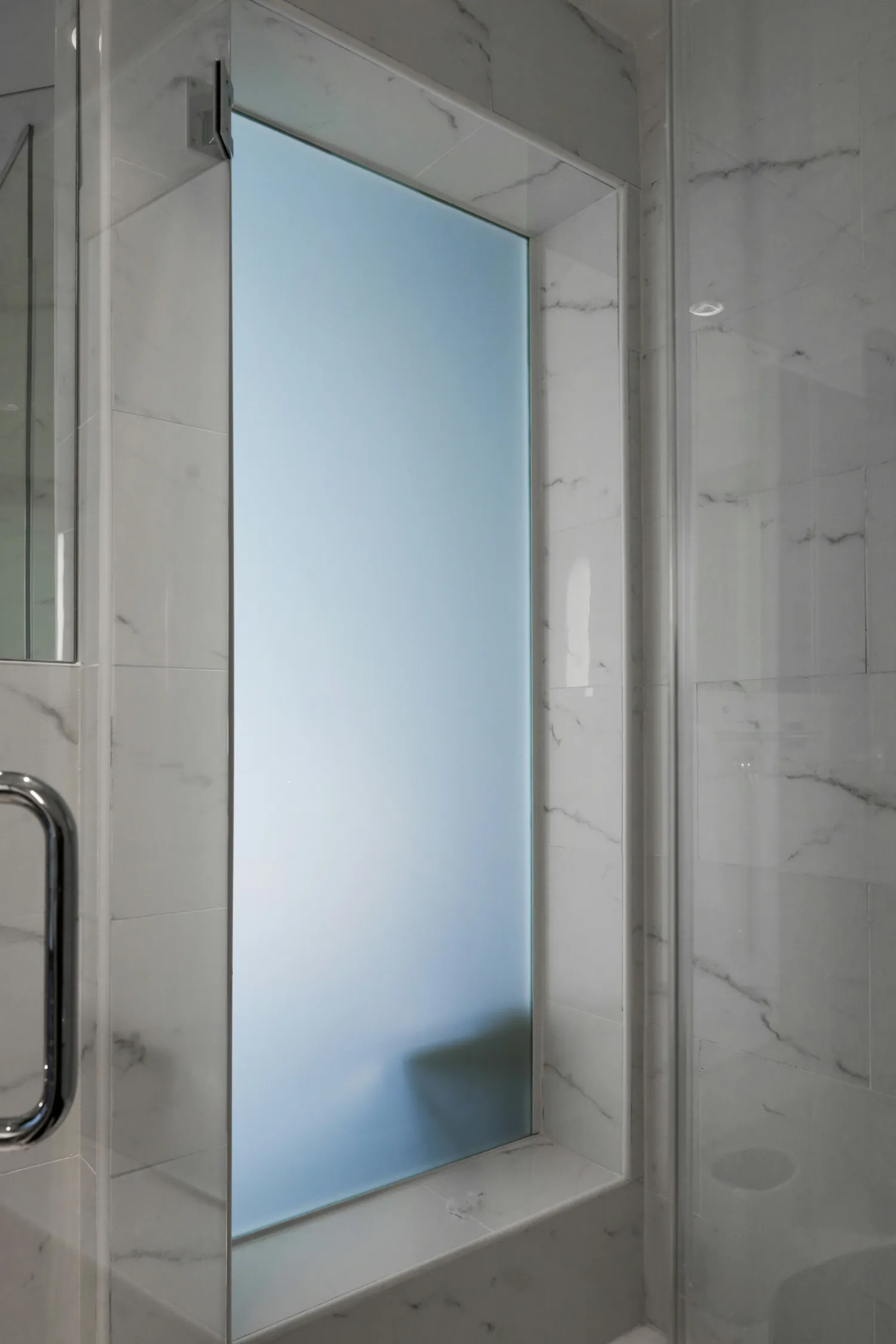 Châssis en verre dépoli dans une douche carrelée de marbre